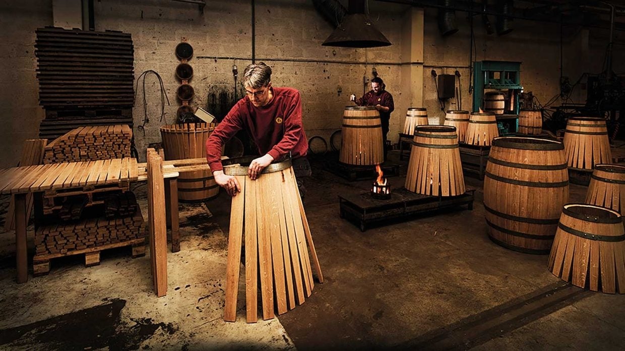 Master cooper examining new oak barrel staves for whiskey production quality control